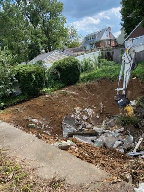 Backyard excavation with a mini excavator, dirt pile, and rubble beside a concrete path