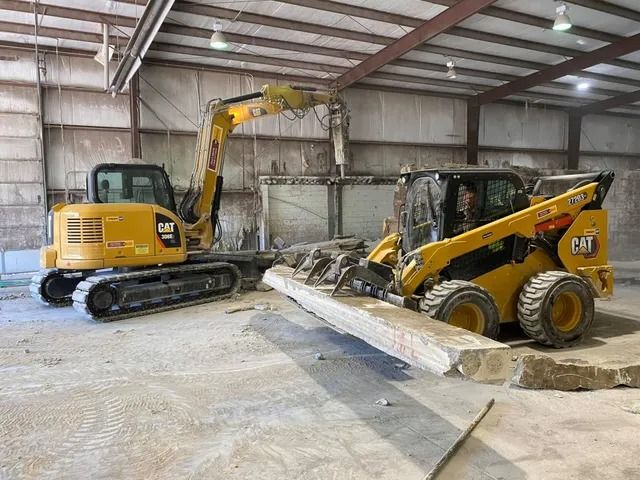 Excavator and skid steer loader moving concrete inside a warehouse construction site.