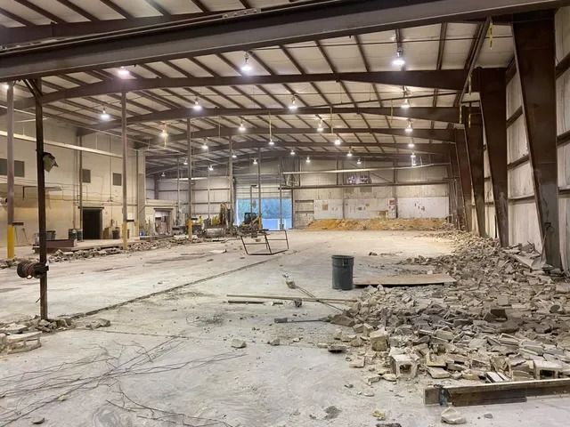 Inside a large empty warehouse under construction, with debris scattered across the concrete floor.