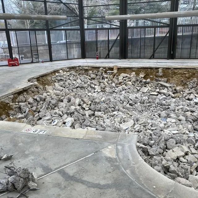 Empty fenced enclosure with a large pit filled with rubble and broken concrete on a wet concrete floor