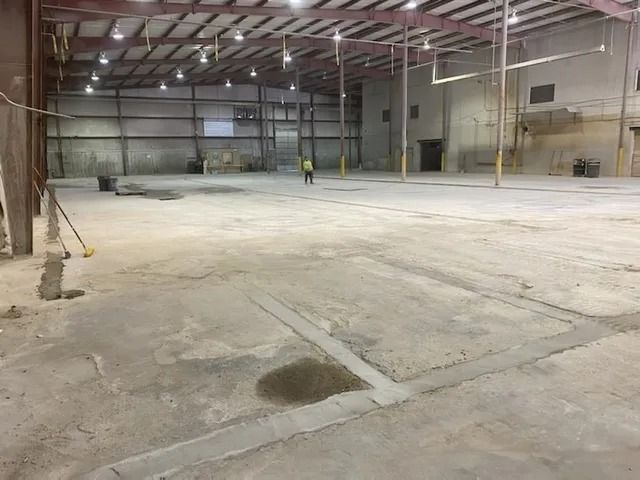 Empty industrial warehouse with concrete floor and a small worker in the distance