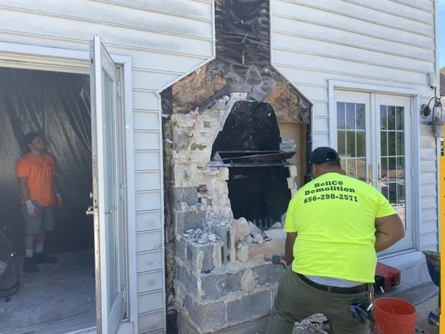 Worker in neon shirt inspecting damaged stone fireplace on a house exterior renovation site