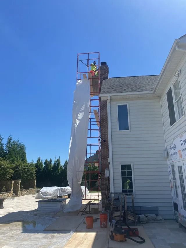 Worker on scaffold beside white house, hanging siding panel under a clear blue sky
