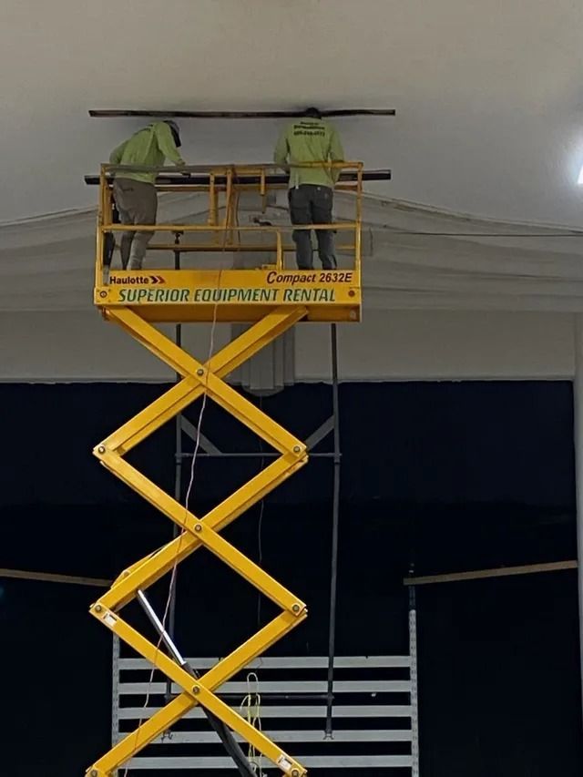 Two workers in yellow safety vests on a raised scissor lift near a ceiling at night