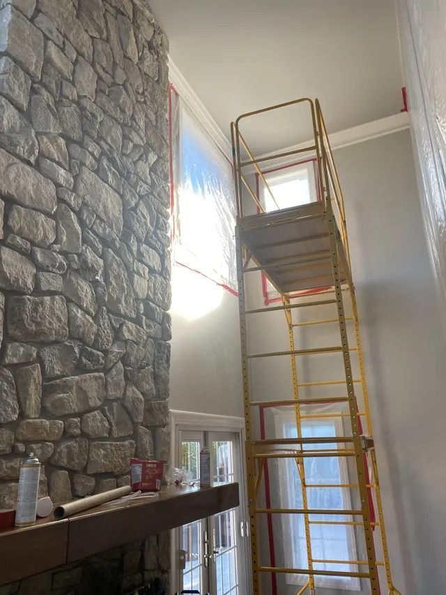 Tall yellow scaffold on an indoor stone-wall fireplace renovation site, with a ladder and bright window light.
