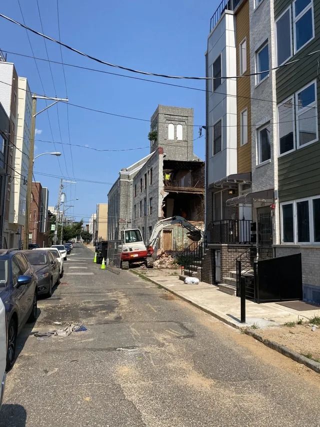 Damaged urban street with parked cars, debris, and a partially collapsed building under a blue sky