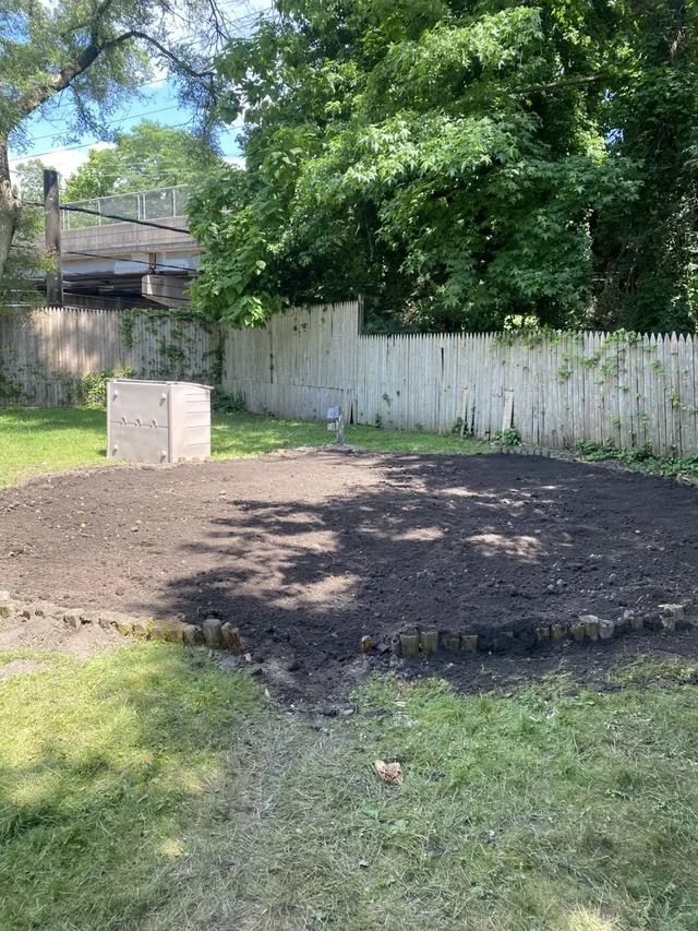 Backyard with a small dirt patch, white fence, and tree shade on a sunny day