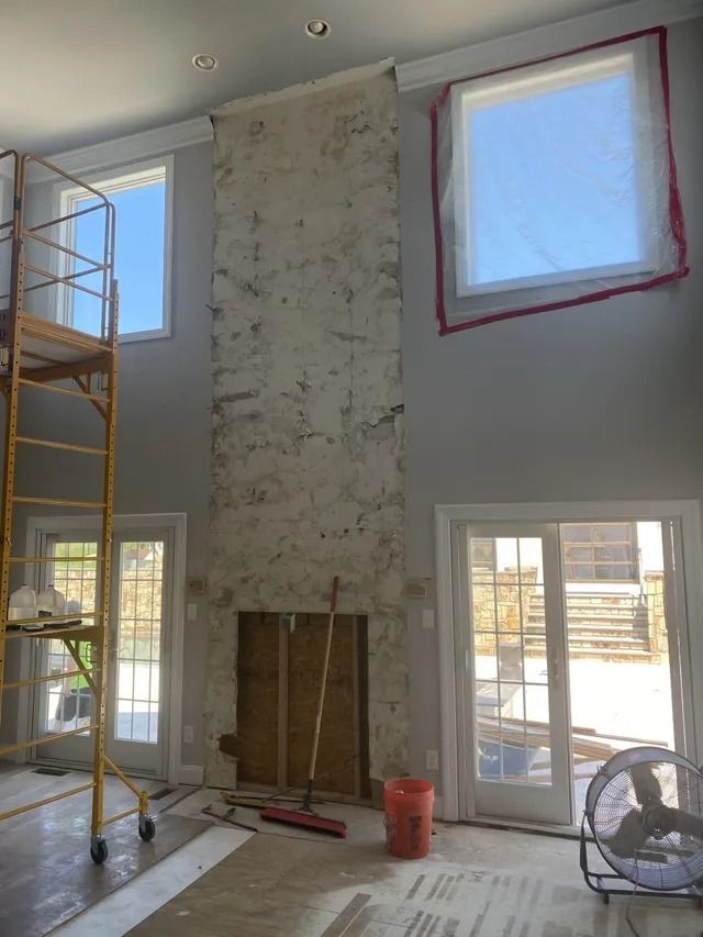 High-ceiling living room under renovation with scaffolding, unfinished wall, and covered window openings