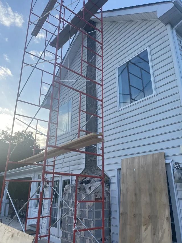 Red scaffold beside a white house with new siding and boarded windows under construction