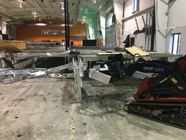 Damaged indoor warehouse with collapsed metal debris and a red tracked machine on the right