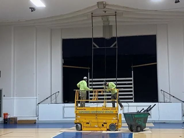 Workers on a stage with a yellow lift and green cart during building maintenance