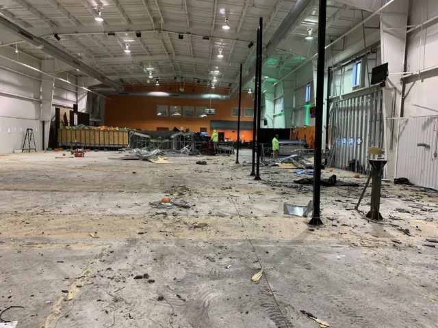 Damaged warehouse interior with debris, broken floor, and exposed beams under bright ceiling lights