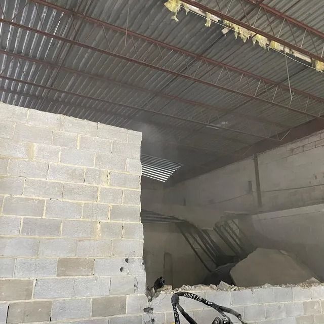 Dim cinderblock warehouse with corrugated metal roof and piles of debris inside