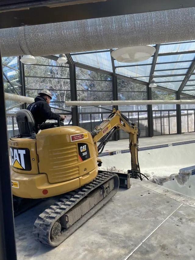 Yellow CAT mini excavator working indoors on a concrete floor under a glass roof.