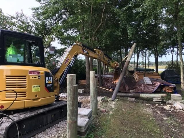 Yellow CAT excavator clearing debris beside a wooded rural area