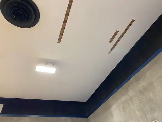 Indoor ceiling with recessed light, black vent, and dark blue trim above gray walls.