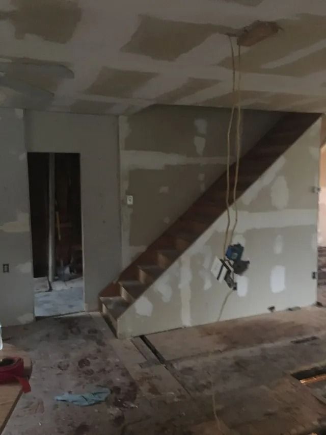 Unfinished room with staircase, drywall patches, exposed floor, and hanging light cord.