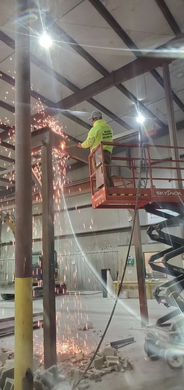 Worker in neon jacket on lift spraying water inside a warehouse under construction