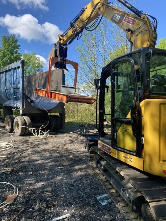 Yellow excavator loading scrap metal into a blue truck in a gravel yard under a blue sky