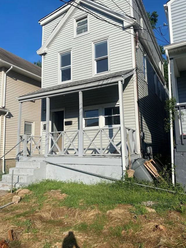 Old white house with a front porch, porch railing, and grass yard in bright sunlight