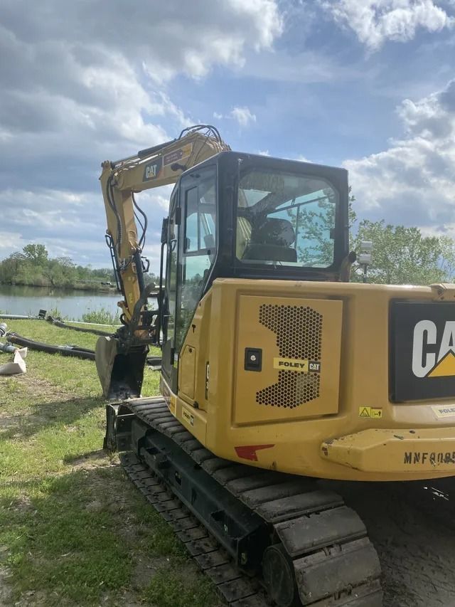 Yellow Caterpillar excavator on tracks beside a waterway under a cloudy sky.