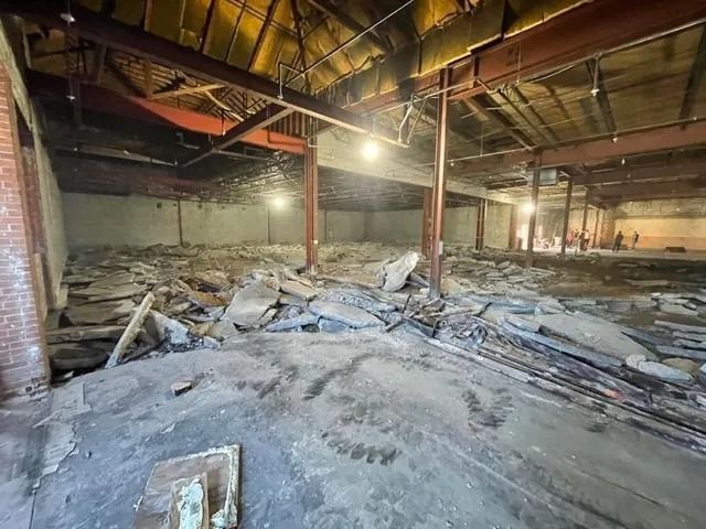 Charred warehouse interior with collapsed debris and steel beams under a damaged roof