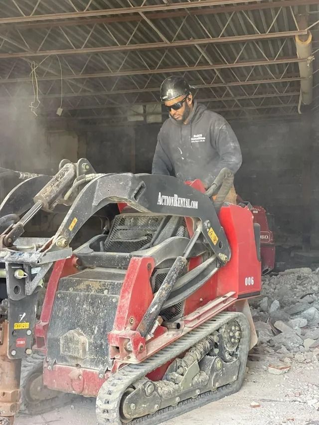 Worker on a red skid steer loader in a dusty barn or workshop.