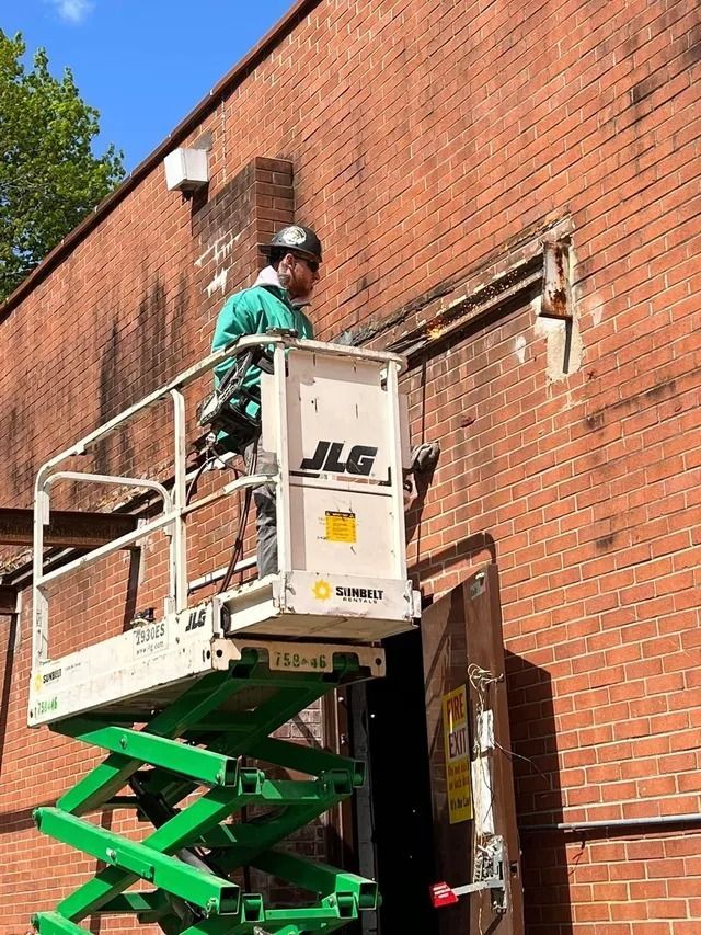 Worker in a green lift repairing a brick wall with a power tool.