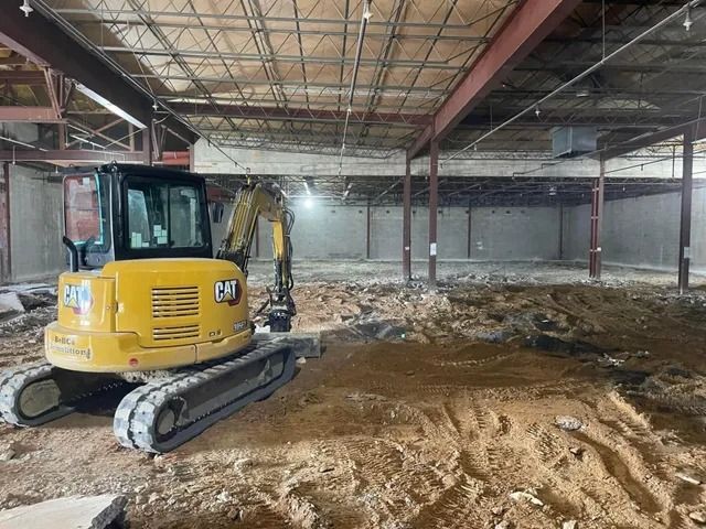 Yellow excavator in a partially demolished warehouse with rubble and exposed steel beams