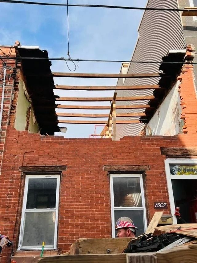 Partially demolished brick building with exposed roof beams and two windows under a blue sky