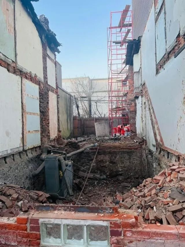 Construction site with demolished walls, rubble, and red scaffolding in a narrow courtyard
