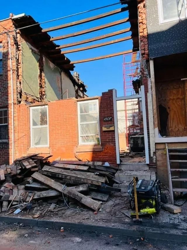 Partially demolished brick house with exposed roof beams and rubble in front