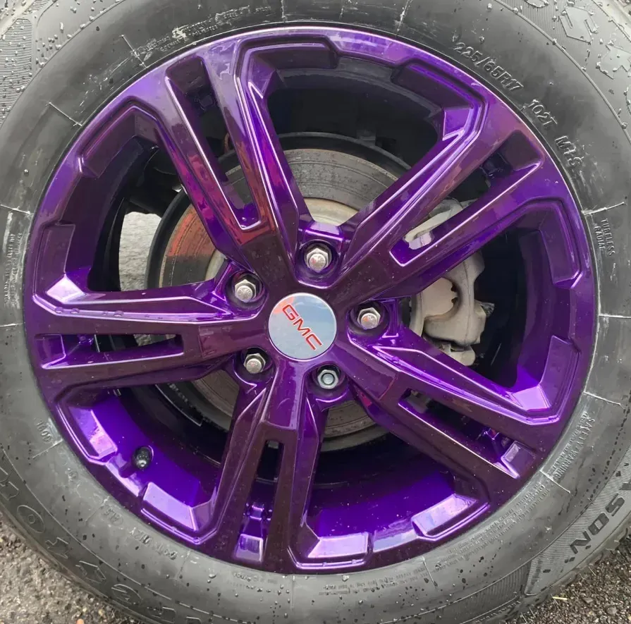 A GMC vehicle wheel with six glossy, deep purple spokes and a matching center cap, fitted with a black tire.
