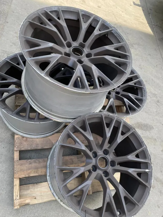 A group of four dark grey, multi-spoke automotive alloy wheels resting on a wooden pallet outdoors.