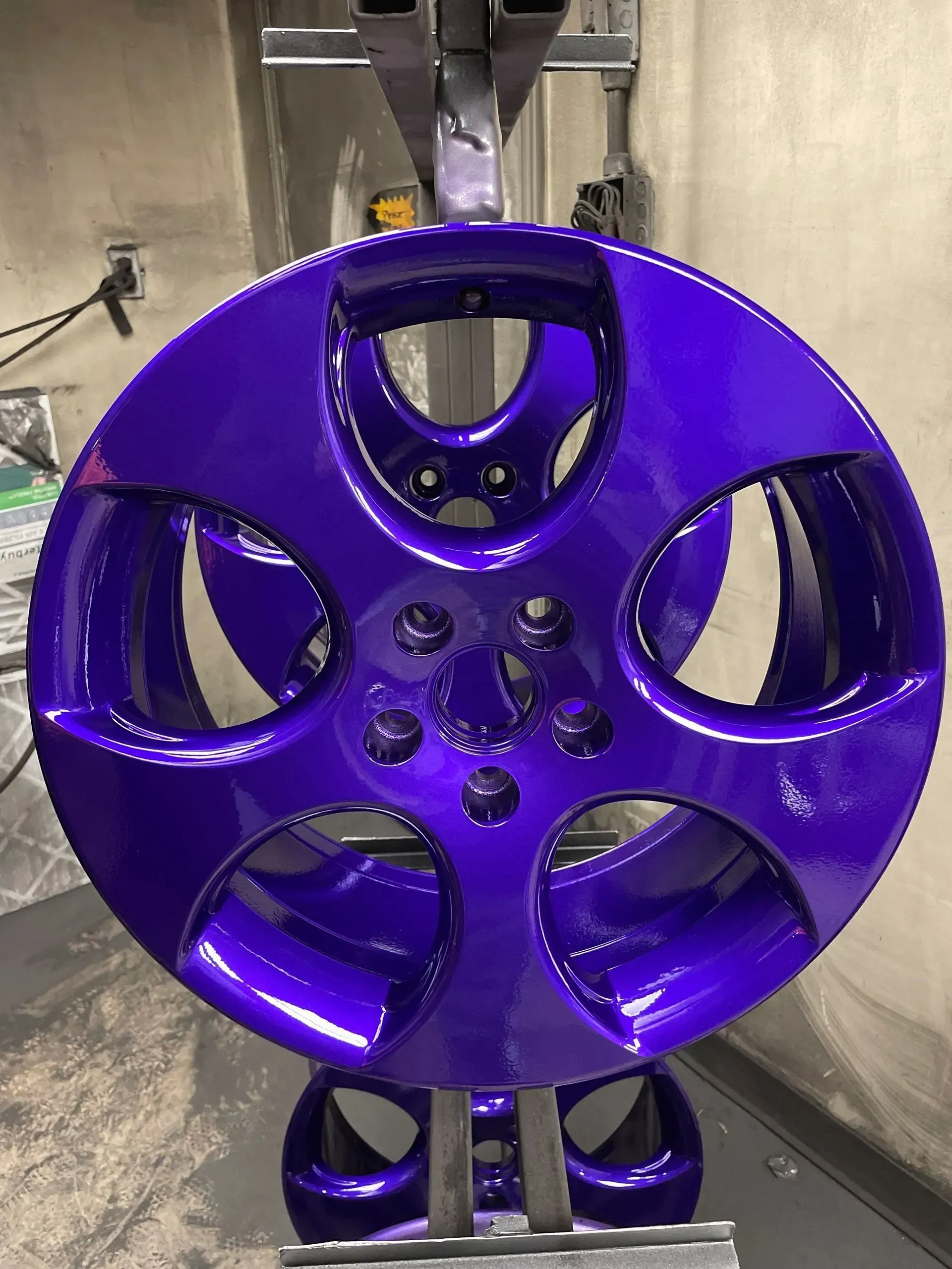A freshly painted, glossy deep-purple automotive wheel rim suspended on a stand in a workshop.
