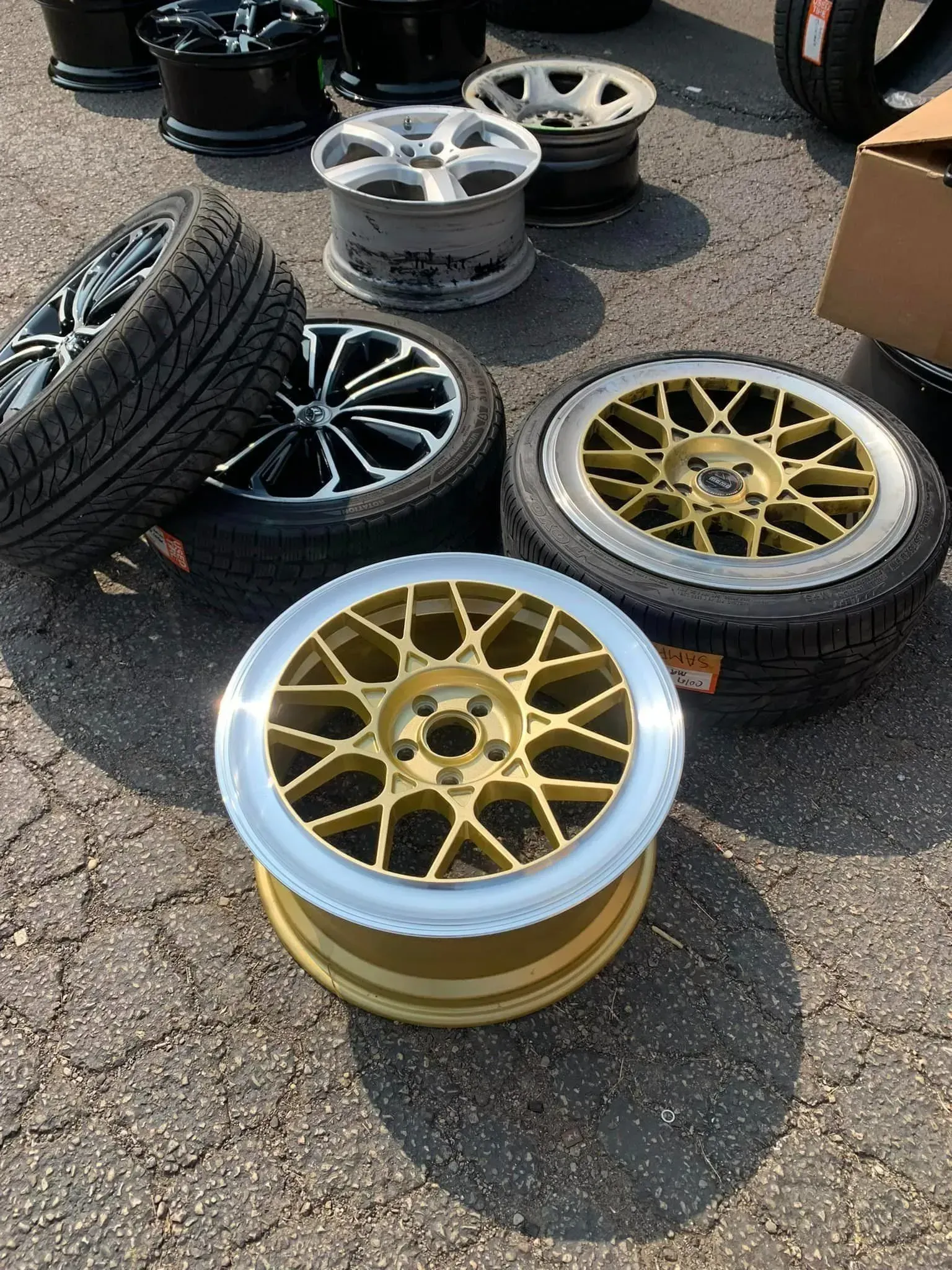 Several car wheels and tires scattered on pavement, including a gold-colored multi-spoke wheel in the foreground.
