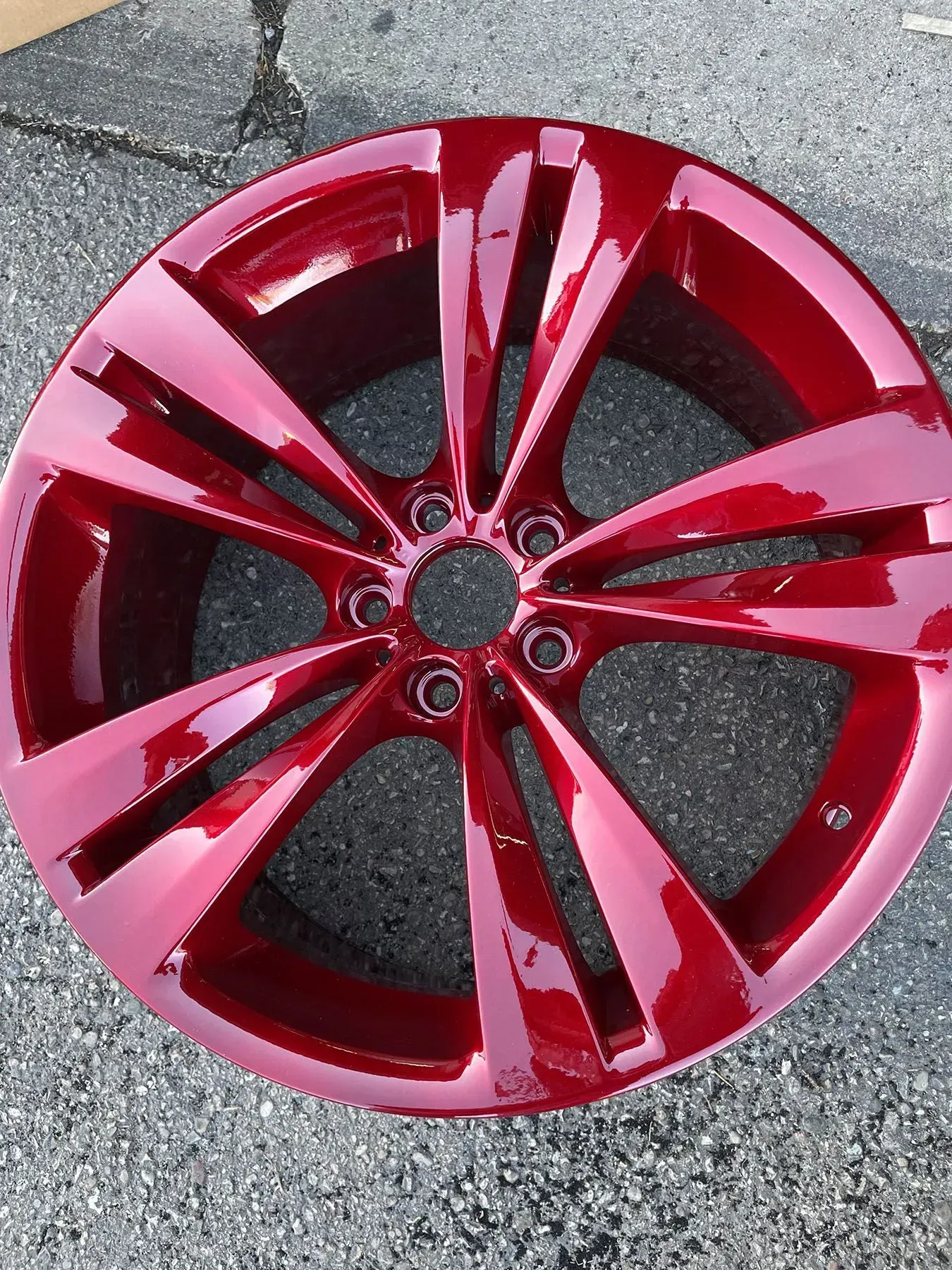A glossy, candy-apple red alloy car wheel with five split spokes, resting on gray asphalt.
