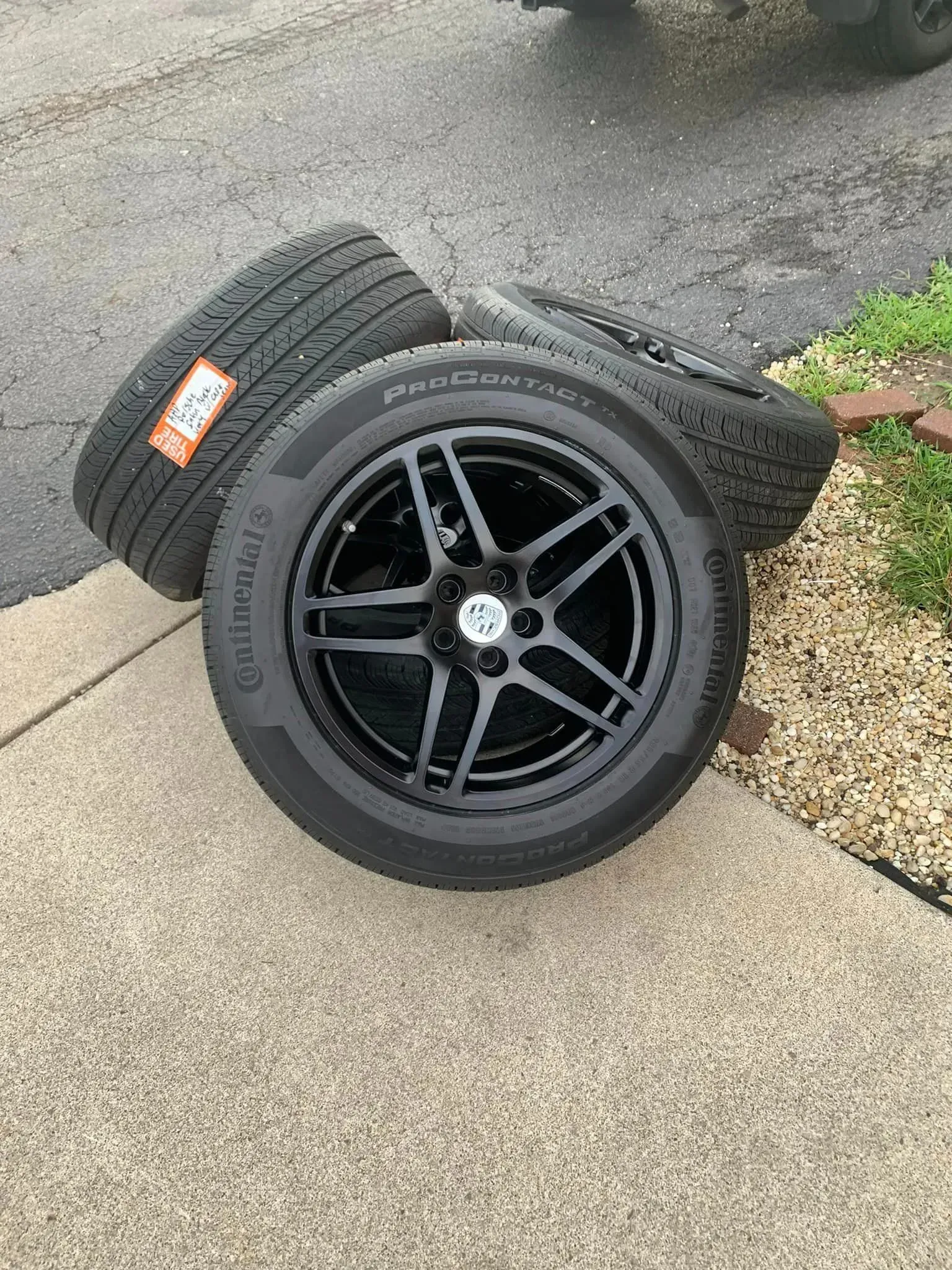 Three black car wheels with Continental tires stacked on a concrete surface outdoors.