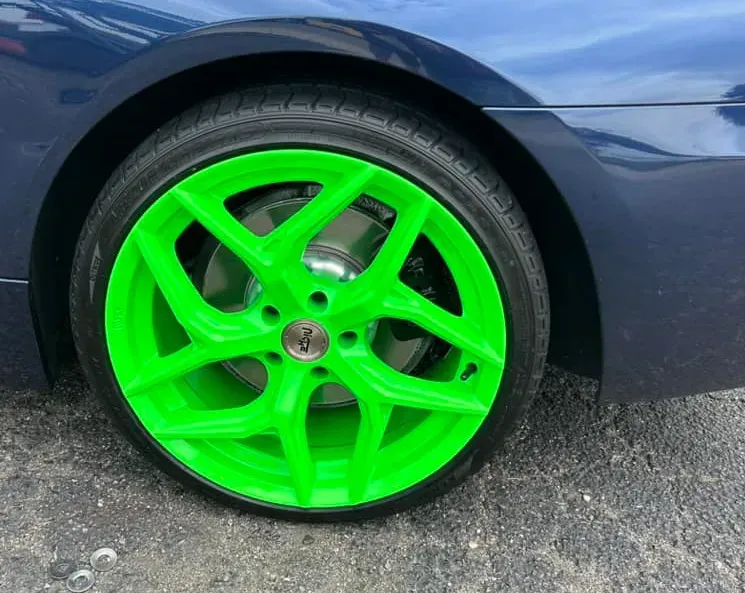 A bright neon green custom alloy wheel on a dark blue car parked on asphalt.