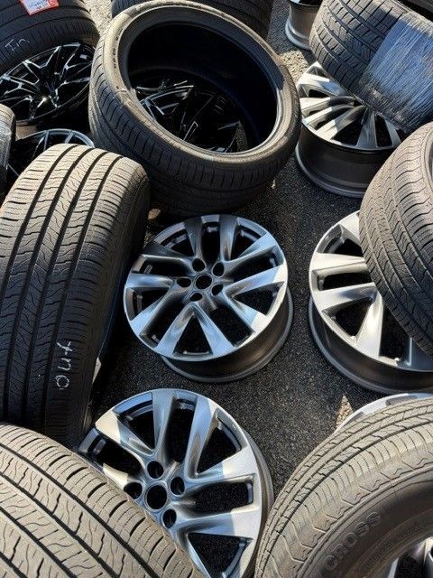 Scattered car tires and silver wheel rims on pavement outdoors