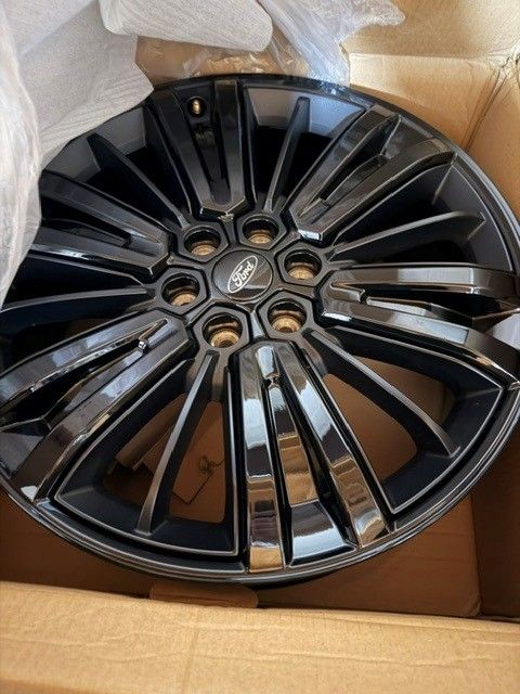 Glossy black multi-spoke alloy wheel rim in a cardboard box