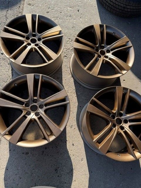 Four bronze alloy car rims arranged on sunlit pavement, seen from above.