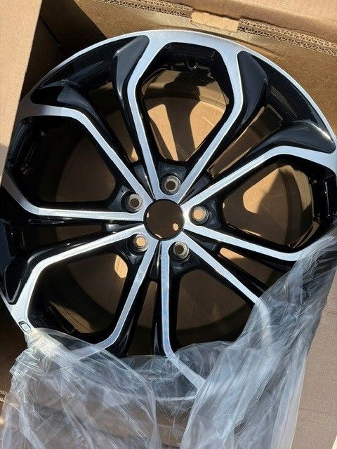 Black and silver car wheel rim in a box, wrapped in clear plastic