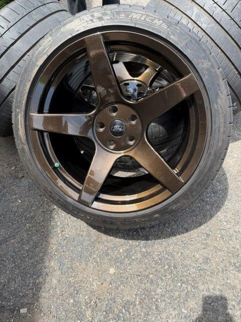 Black five-spoke car wheel tire lying on pavement, close-up view