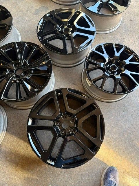 Several black and silver alloy car rims displayed on a floor, viewed from above