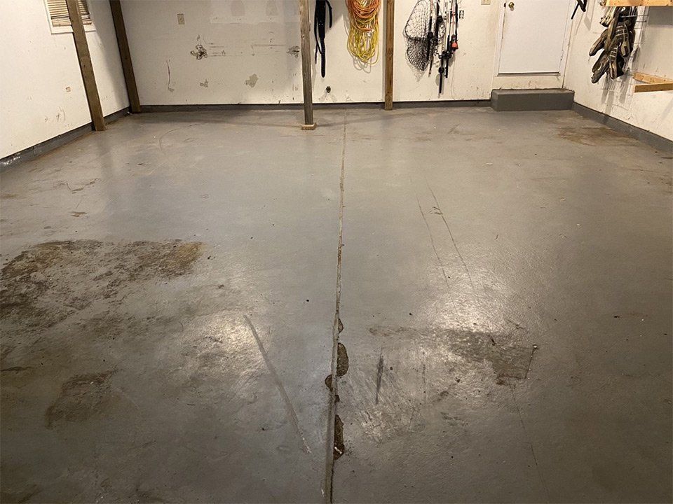 A gray concrete garage floor with a central expansion joint and areas of wear and staining.