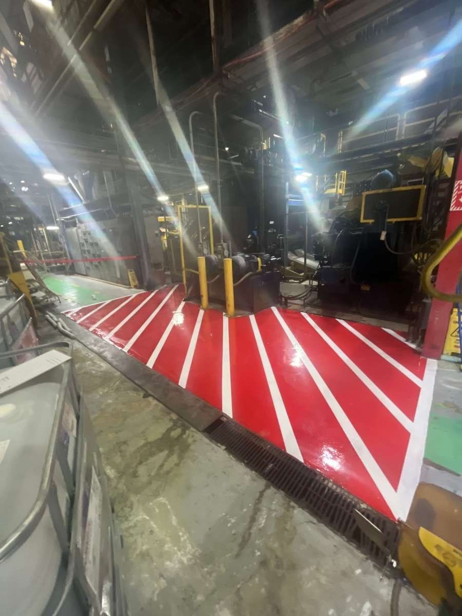 A high-angle view of a factory floor marked with red and white diagonal safety stripes near machinery.