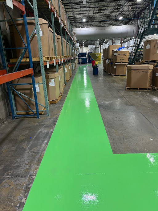 Warehouse aisle with bright green floor marking and shelving on both sides.
