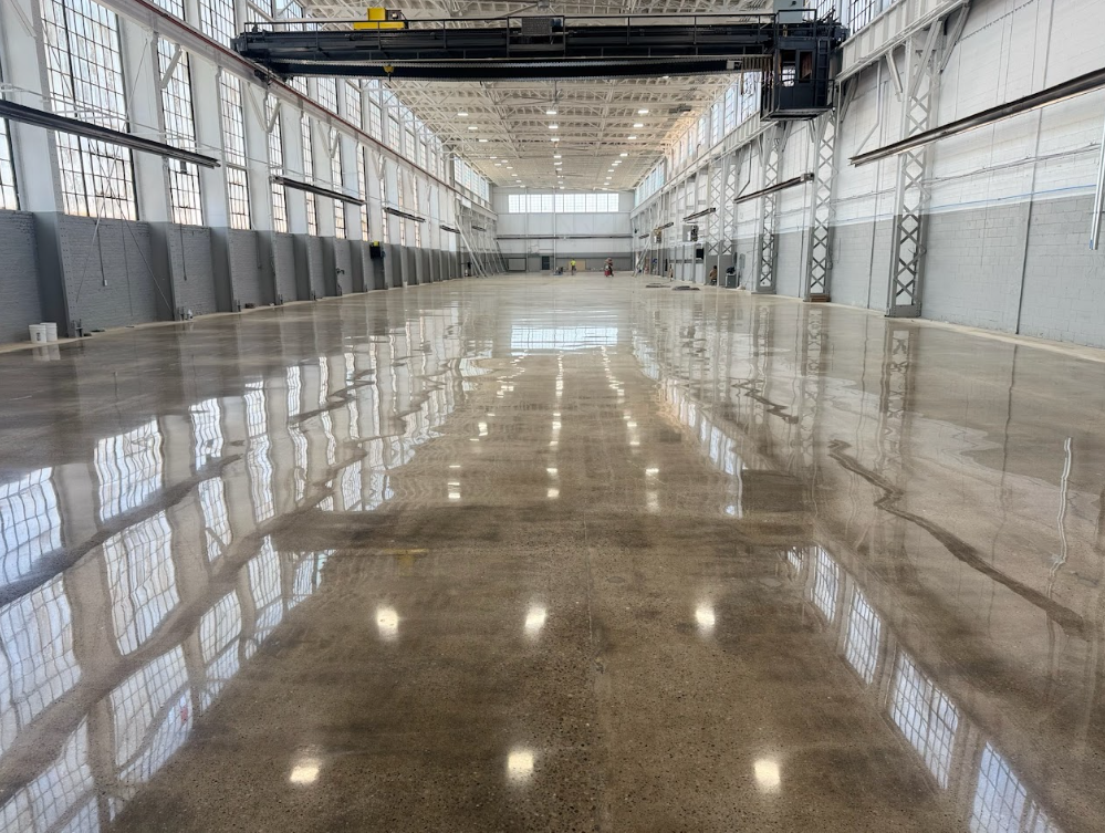 Empty industrial warehouse with a polished reflective floor and overhead crane walkway.