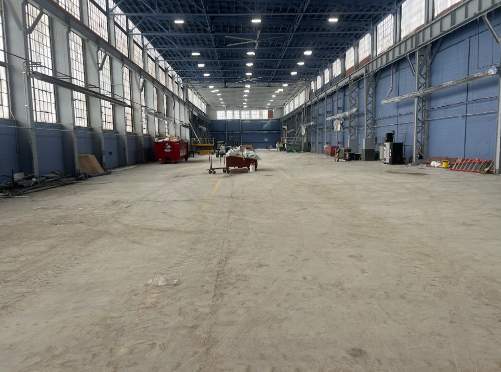 An empty industrial warehouse with a high, arched ceiling, large windows, and a concrete floor.